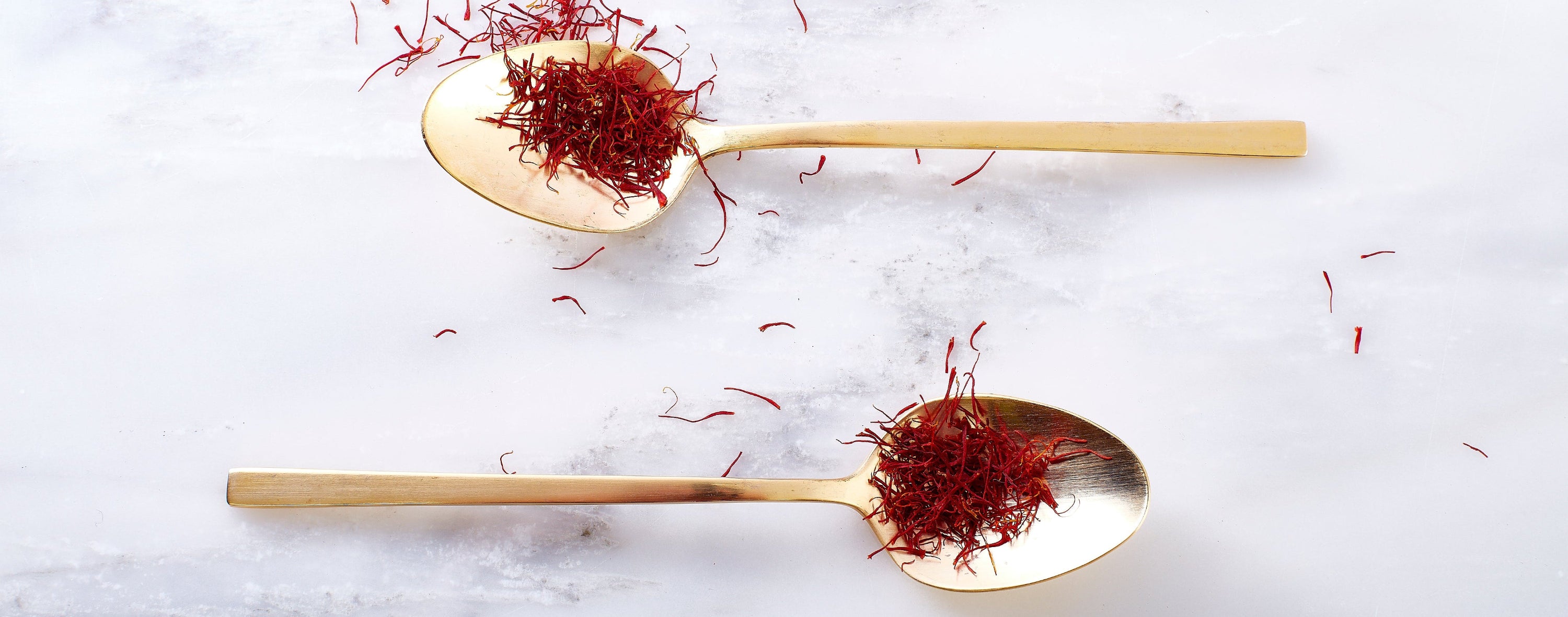 Two gold spoons with saffron on a white marble surface